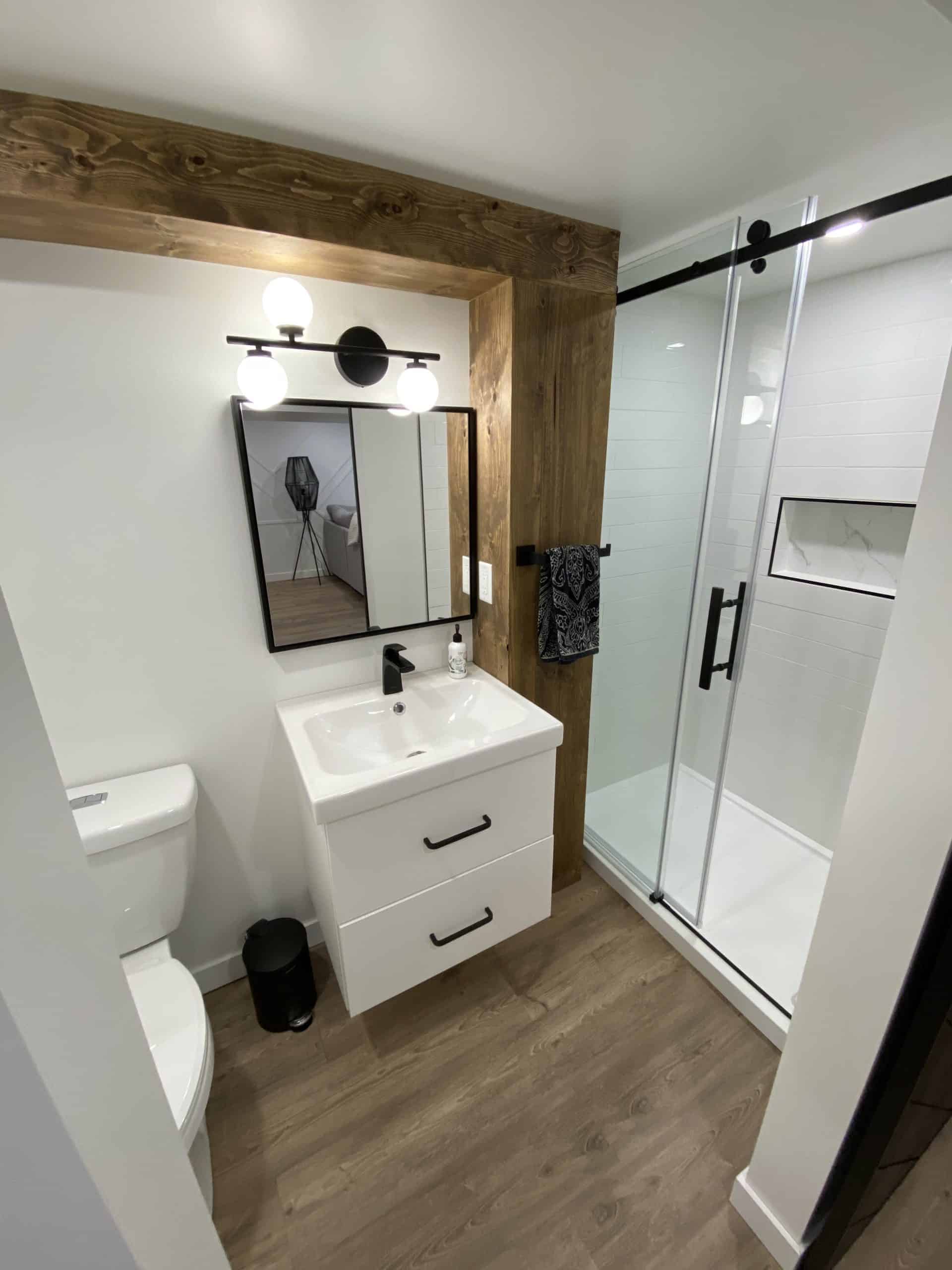 white and black basement bathroom with wood accent covering plumbing conduit