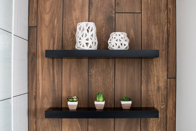 two black floating shelves in bathroom on wood accent wall