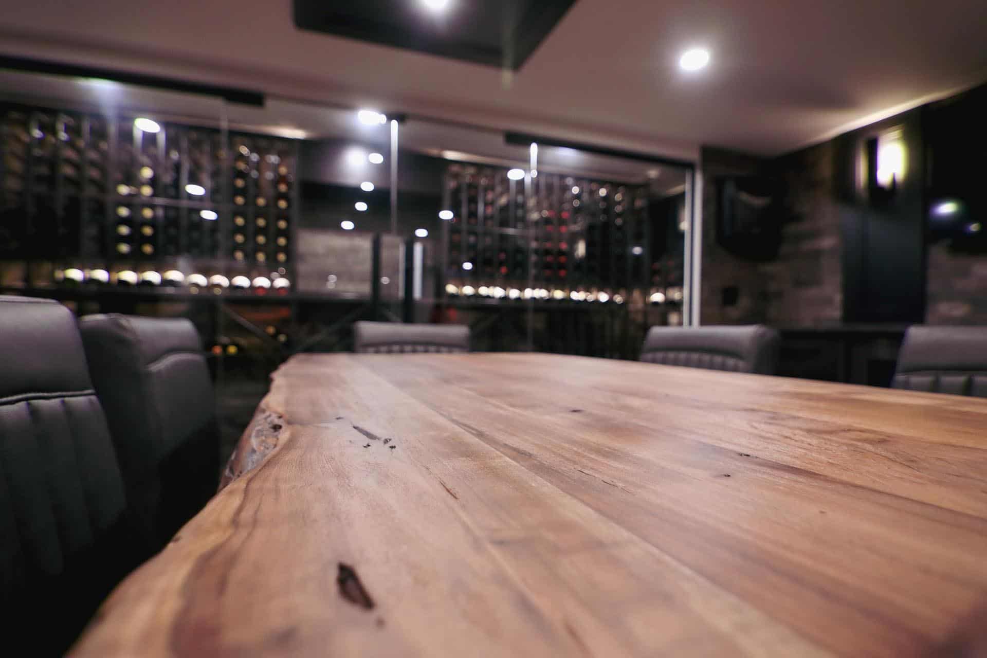 clean wooden table top in a beautiful dining room with wine display rack in background