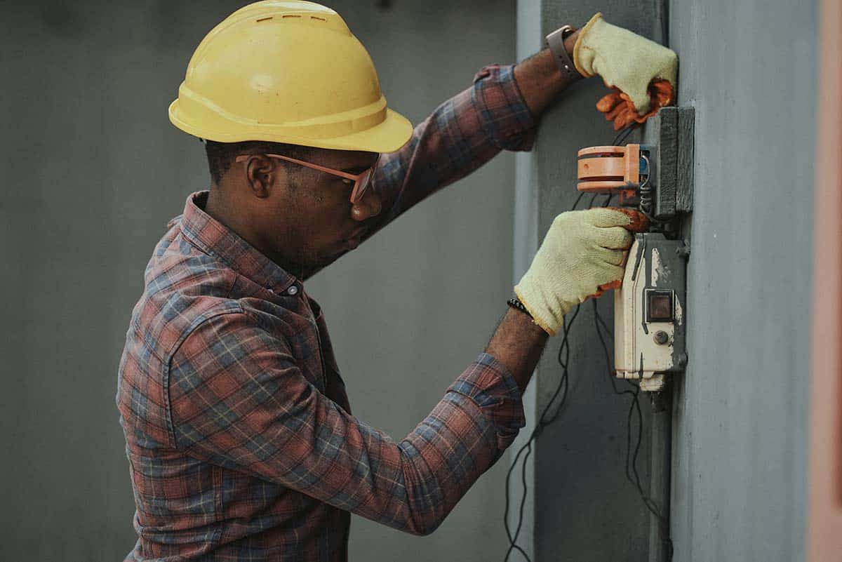 tradesperson in hard hat and gloves working on electrical box