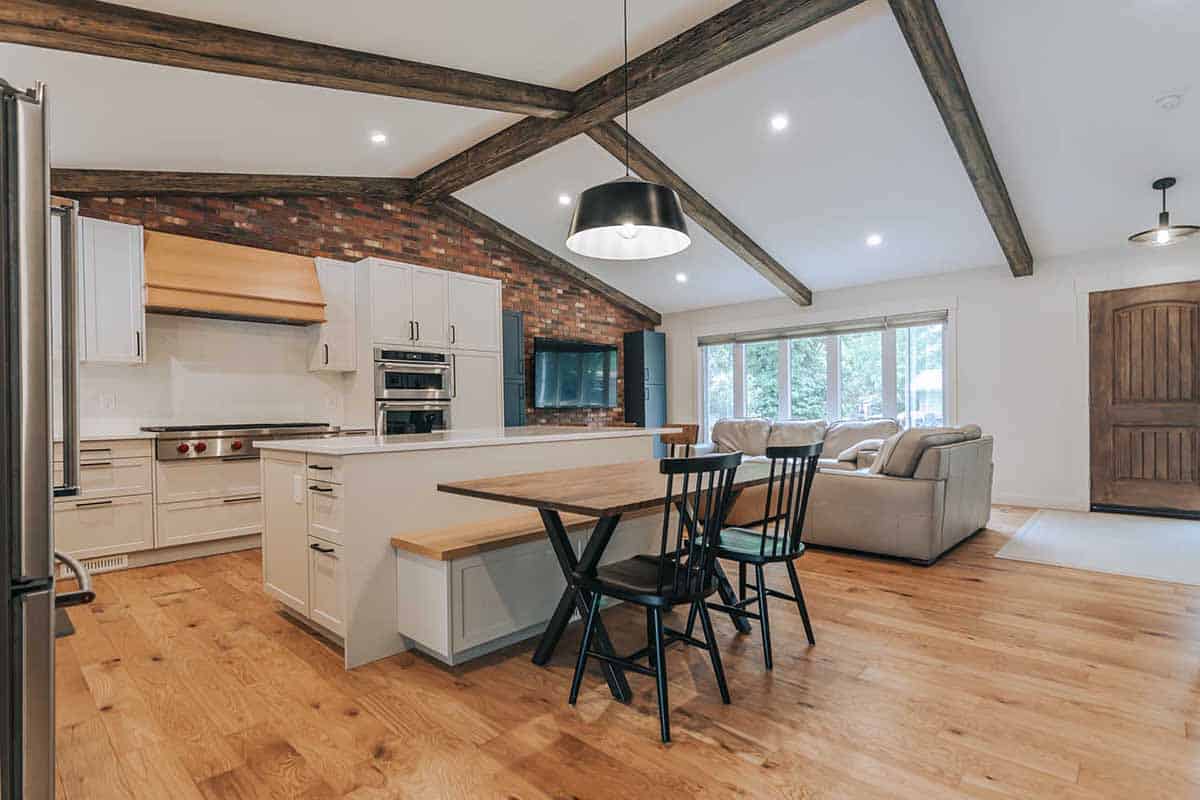hardwood flooring in wide concept kitchen and living room with brick accent wall and exposed wooden beams