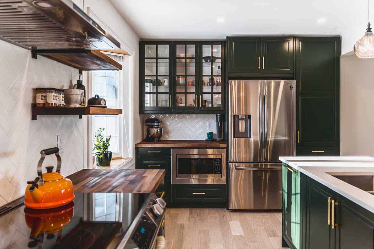 light laminate flooring in kitchen with dark green cabinets, butcher block countertop and gold hardware