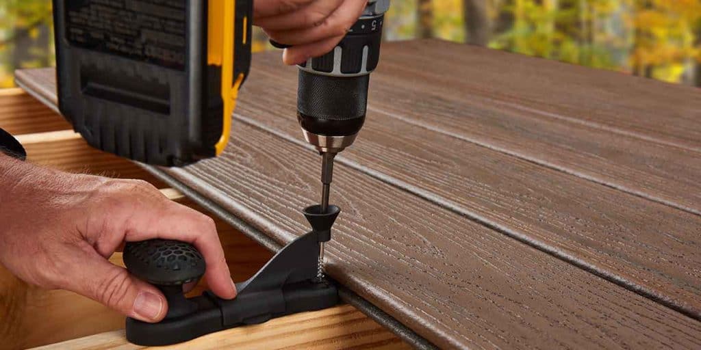 Close up of hands and a drill installing a brown colored composite deck