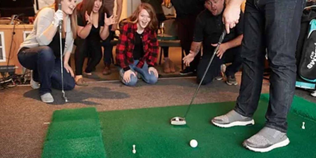 a man putting at an indoor golf event with his friends cheering him on in the background